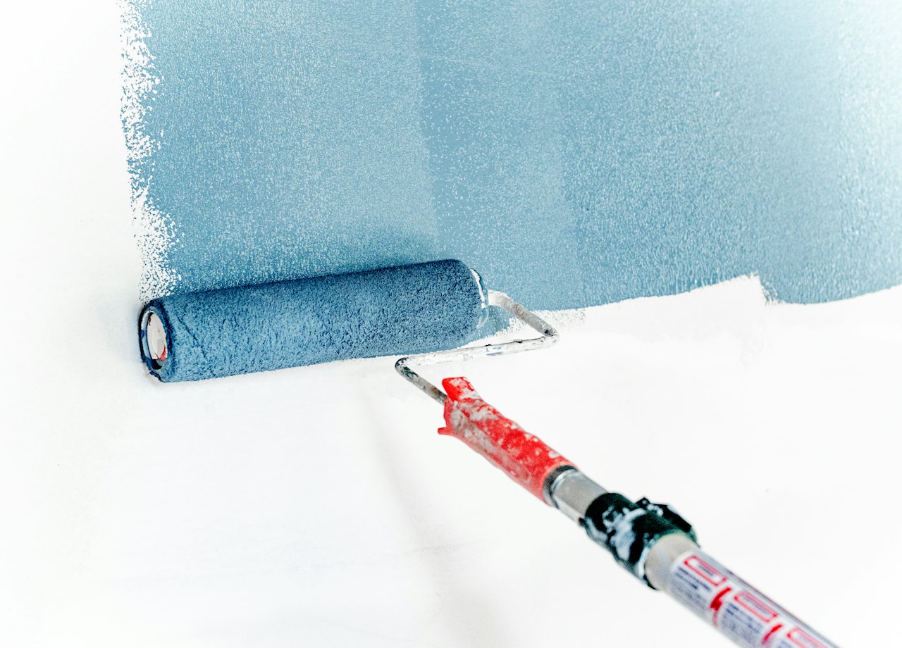 Paint roller laying fresh blue paint onto a white wall