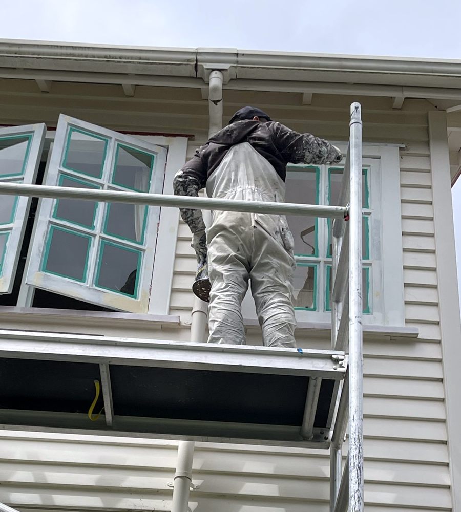 VN Painting & Decoration painter on scaffolding sanding and priming masked timber windows on a weatherboard house